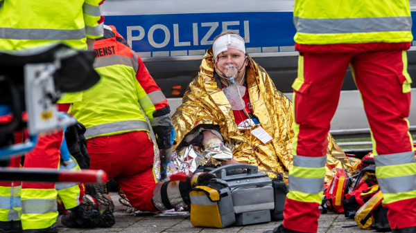 Notfallsanitäter versorgen einen verletzten Menschen mit Kopfverband und Sauerstoffmaske vor einem Polizeistreifenwagen und Notfallausrüstung