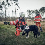 Eine Ehrenamtliche der Rettungshundestaffel weist einem Hund die Richtung.