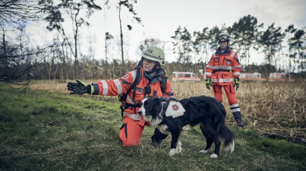 Eine Ehrenamtliche der Rettungshundestaffel weist einem Hund die Richtung.