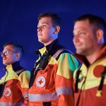 Notfallreform: Drei Einsatzkräfte des DRK-Rettungsdienstes in orange-gelber Warnkleidung vor blauem Hintergrund